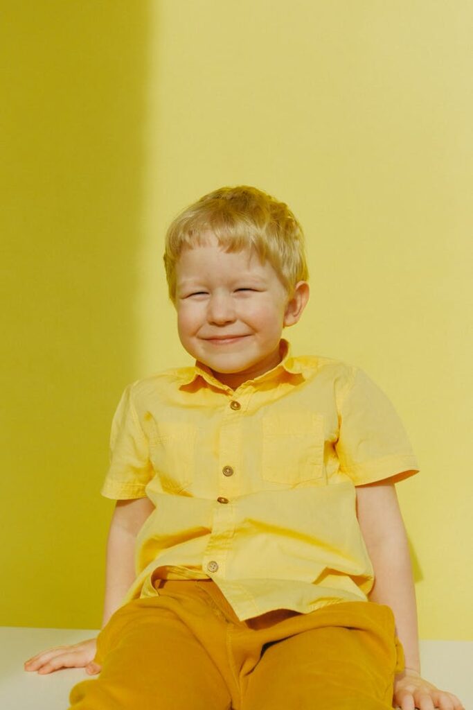 A joyful child dressed in yellow sits against a vibrant yellow background, exuding happiness.