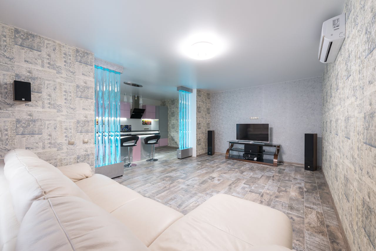 services-01 Comfortable white sofa placed in spacious room with TV and decorative colorful bubble wall near modern kitchen in stylish apartment
