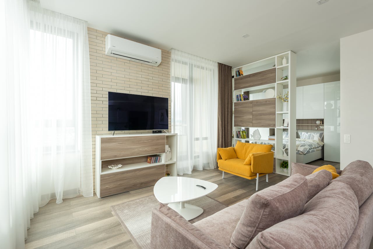services-03 Cozy sofa and armchair placed near cabinet with TV set in contemporary living room separated from bedroom with cupboard and shelves in spacious studio apartment